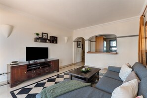 Una sala moderna con televisor de pantalla plana, mueble de entretenimiento de madera oscura, sofá gris y una alfombra estampada.