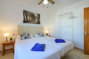 A double bed with white bedding, two bedside tables with lamps, a wall-mounted painting, and a wooden door. - Holiday Apartment Casa Veronica with Shared Pool & Private Terrace (Playa Blanca)