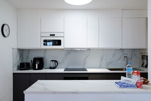 A modern kitchen with white cabinets, a microwave, a coffee maker, and a sink.