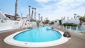 Une piscine dotée d’une plage blanche, entourée de palmiers et de bâtiments blancs.
