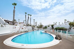 Ein Swimmingpool mit weißem Sonnendeck, umgeben von Palmen und weißen Gebäuden.