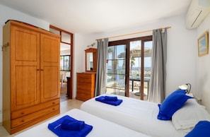 Une chambre d’hôtel avec deux lits, une armoire, une commode, un miroir et un balcon avec vue sur la mer.