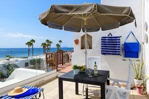 Een terras met een tafel, stoelen, een fles en uitzicht op zee.