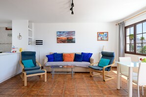 Een woonkamer met een bank, twee fauteuils, een salontafel en een eethoek met een glazen tafel en stoelen.