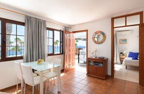 Una habitación con una mesa de comedor, sillas, un armario, una cama y vistas al mar a través de las ventanas.