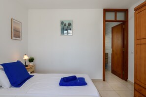 Een hotelkamer met een bed, een nachtkastje met een lamp en een plant, een schilderij aan de muur en een houten garderobe.