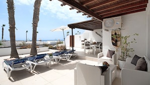 Un’area salotto esterna coperta con poltrone, un tavolo e una pianta in vaso.