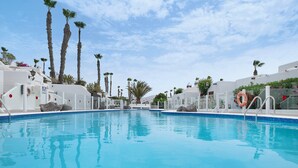 Una piscina cristallina blu con edifici bianchi e palme sullo sfondo.