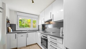 A modern kitchen with white cabinets, a built-in oven, and a window with a view of greenery. - Panoramic Sea View Villa with Large Terrace, Shared Pools & Space for 8 (Almunecar)