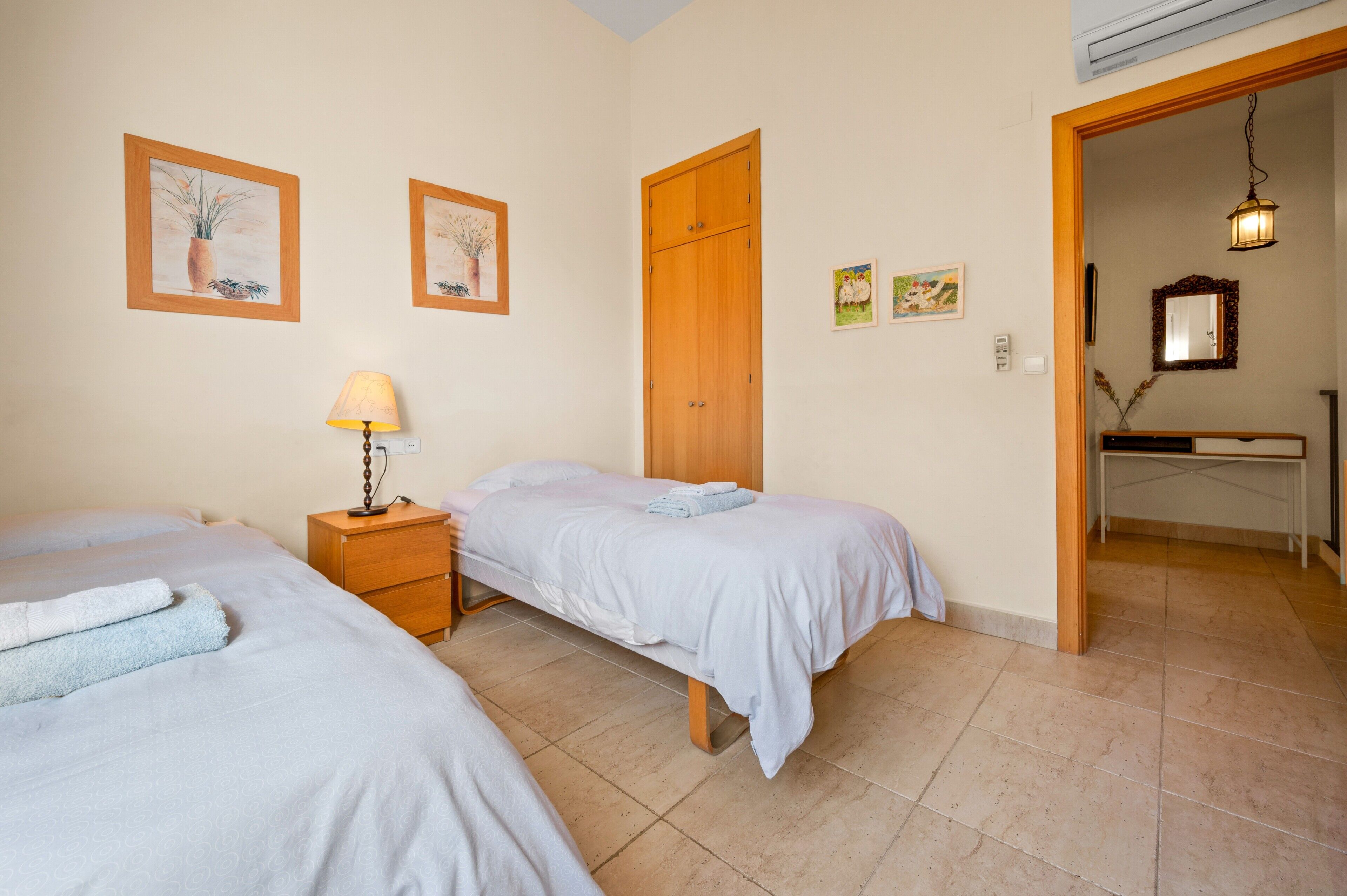 Une chambre avec deux lits, une armoire en bois, une table de chevet avec une lampe et un petit bureau avec un miroir.
