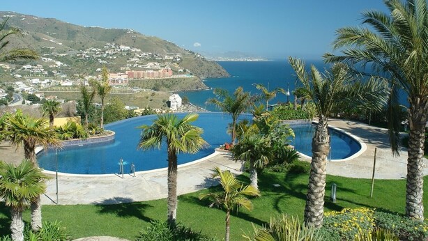 A resort with a large infinity pool, palm trees, and a view of the coastline. - Panoramic Sea View Villa with Large Terrace, Shared Pools & Space for 8 (Almunecar)