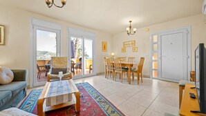 A spacious living area with a sofa, coffee table, and dining set. There are large sliding glass doors leading to an outdoor patio. - Panoramic Sea View Villa with Large Terrace, Shared Pools & Space for 8 (Almunecar)