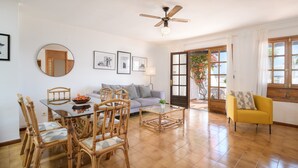 A living room with a dining table, chairs, a sofa, a yellow armchair, a ceiling fan, and a large window with a view. - Apartment "Puerto Chico 7" with Sea View, Shared Pool, Terrace & Wi-Fi (Playa Blanca)