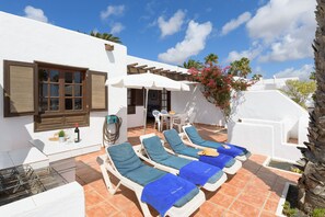 Un bâtiment blanc doté d’un patio aménagé avec des chaises longues, une table et un barbecue.