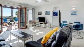 Een woonkamer met een bank, televisie en een eethoek met stoelen.