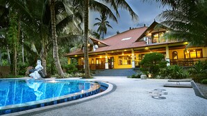 A resort with a swimming pool, palm trees, and a building with a tiled roof. - Camplung Beach Villa and Farmstead (Tejakula)