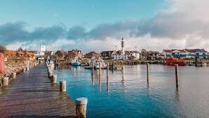 A wooden pier leading to a harbor with boats, a lighthouse, and residential buildings. - Gemütlicher Bungalow mit Garten (Insel Poel)