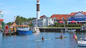 A harbor with boats, a lighthouse, and buildings with red roofs. - Gemütlicher Bungalow mit Garten (Insel Poel)