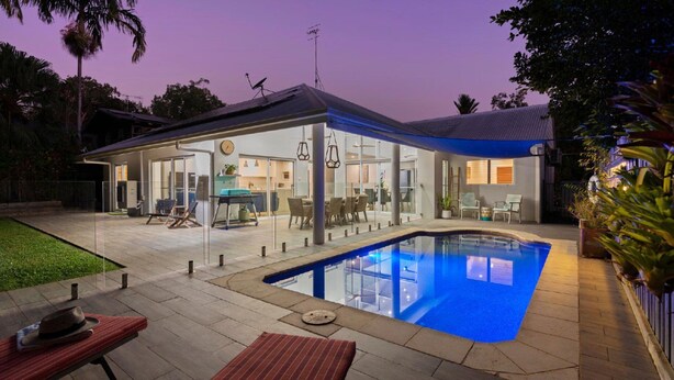 A modern house with a glass-enclosed patio, a swimming pool, and a dining area.