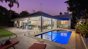 Una moderna casa con patio in vetro, piscina e zona pranzo.