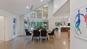 A spacious, modern kitchen with a large island, a dining area with a table and chairs, and a view of the outdoors through large windows.