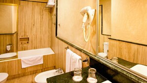 Un baño con tocador de madera, un lavabo blanco, un espejo, un perchero para toallas y un secador de pelo.