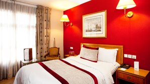 Una habitación de hotel con una cama, lámparas de noche, un escritorio, una silla y un cuadro en la pared.