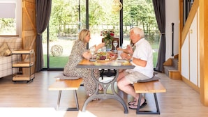 Uma área de refeições com uma mesa posta para dois, um banco de madeira e vista para o verde lá fora.