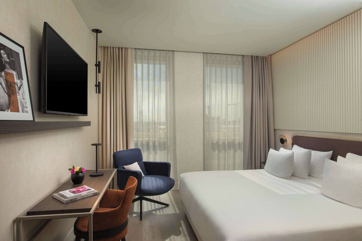 A hotel room with a bed, a desk with a chair, a television, and a window with curtains.