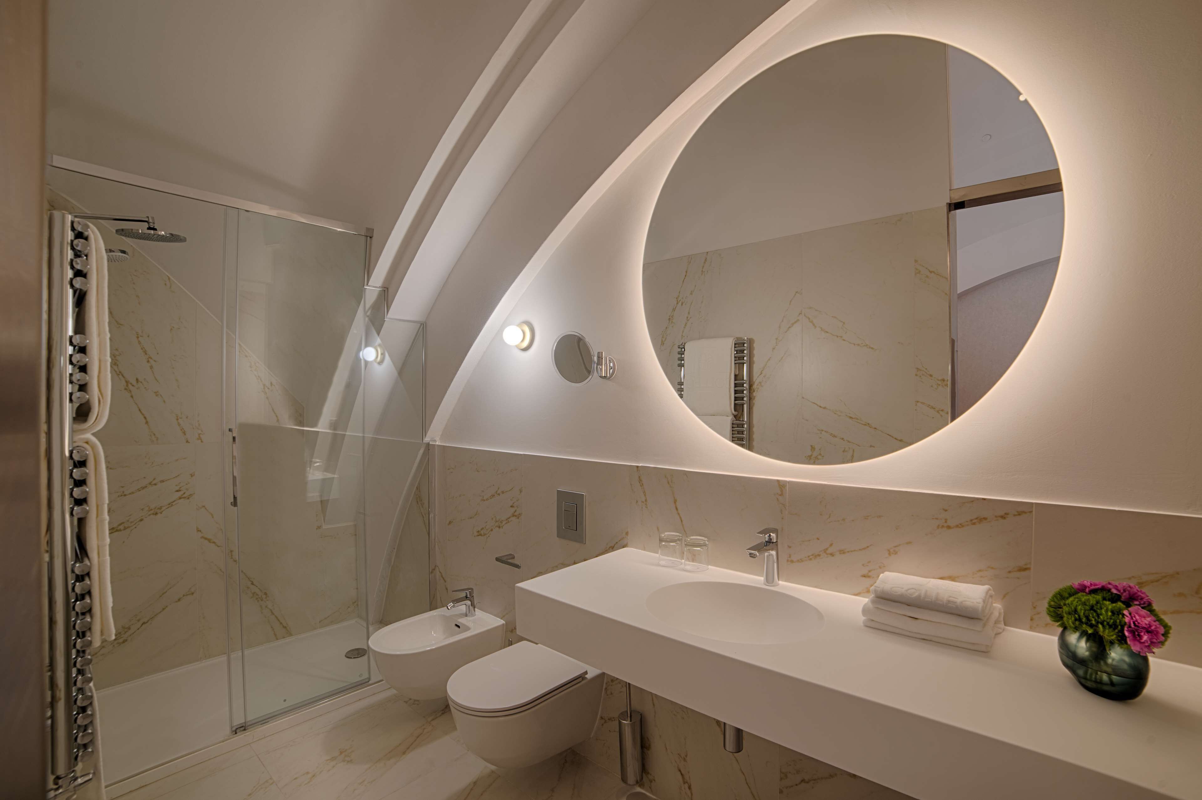 Ein modernes Badezimmer mit einer gläsernen Duschkabine, einem weißen Waschbecken und einem großen Spiegel.