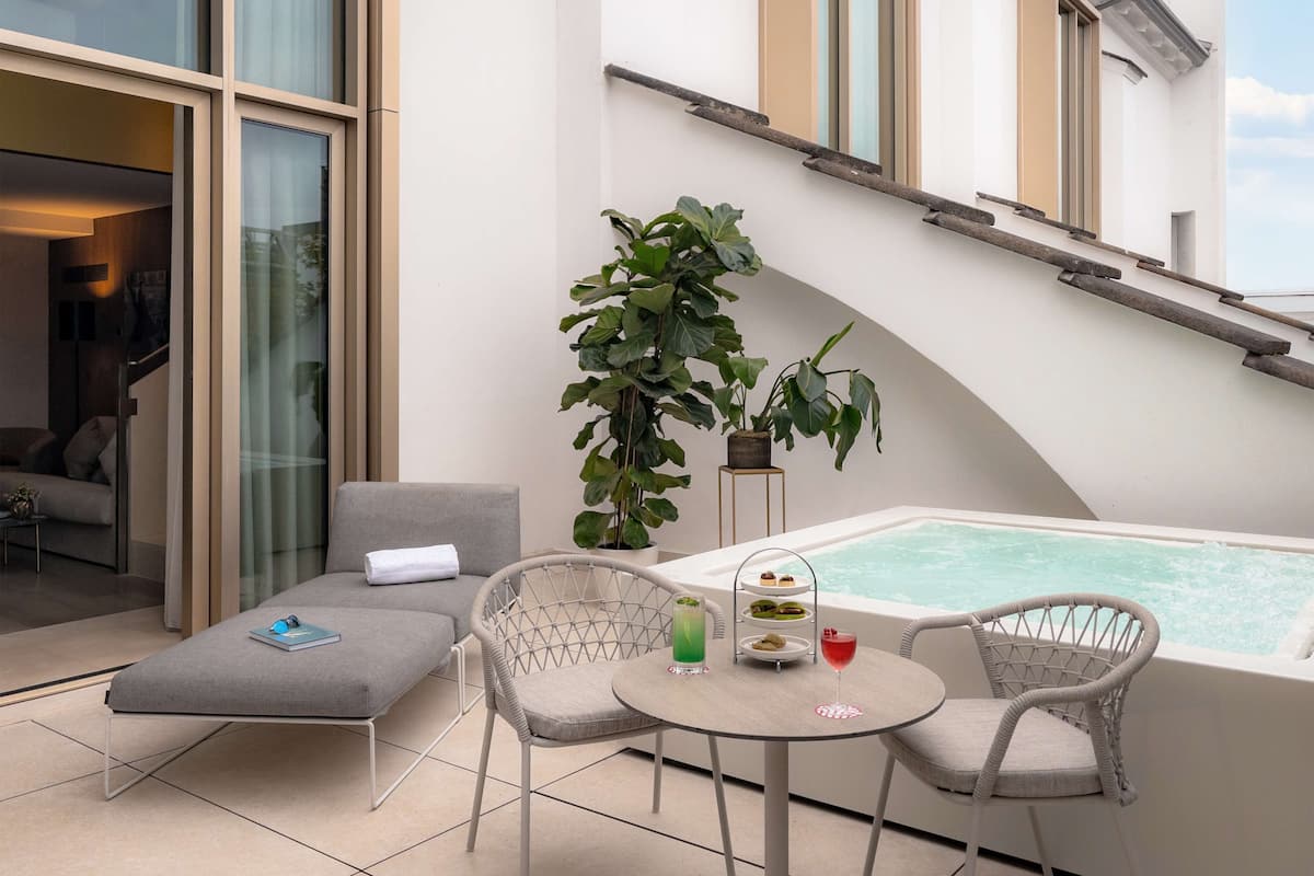 A modern outdoor seating area with a pool, lounge chairs, and a small table with drinks.