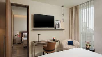 A hotel room with a bed, a desk with a chair, a TV mounted on the wall, and a window with curtains.