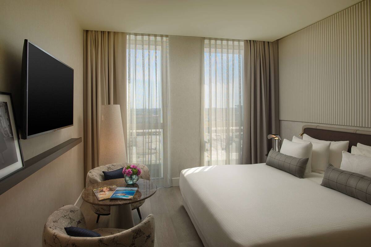 A hotel room with a bed, a TV, a desk with a chair, and a window with curtains.