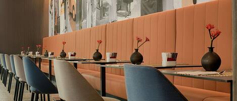 A row of dining tables with chairs, each table has a vase with red flowers, and the walls are adorned with large black and white photographs.