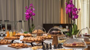 Ein Buffet mit verschiedenen Gebäcken und Desserts, darunter Croissants und Muffins, präsentiert auf Holzständern und unter Glaskuppeln.