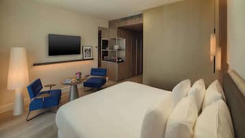 Ein Hotelzimmer mit einem großen Bett, einem an der Wand befestigten Flachbildfernseher, einem Schreibtisch mit Stuhl, einer Lampe und einem Bücherregal.