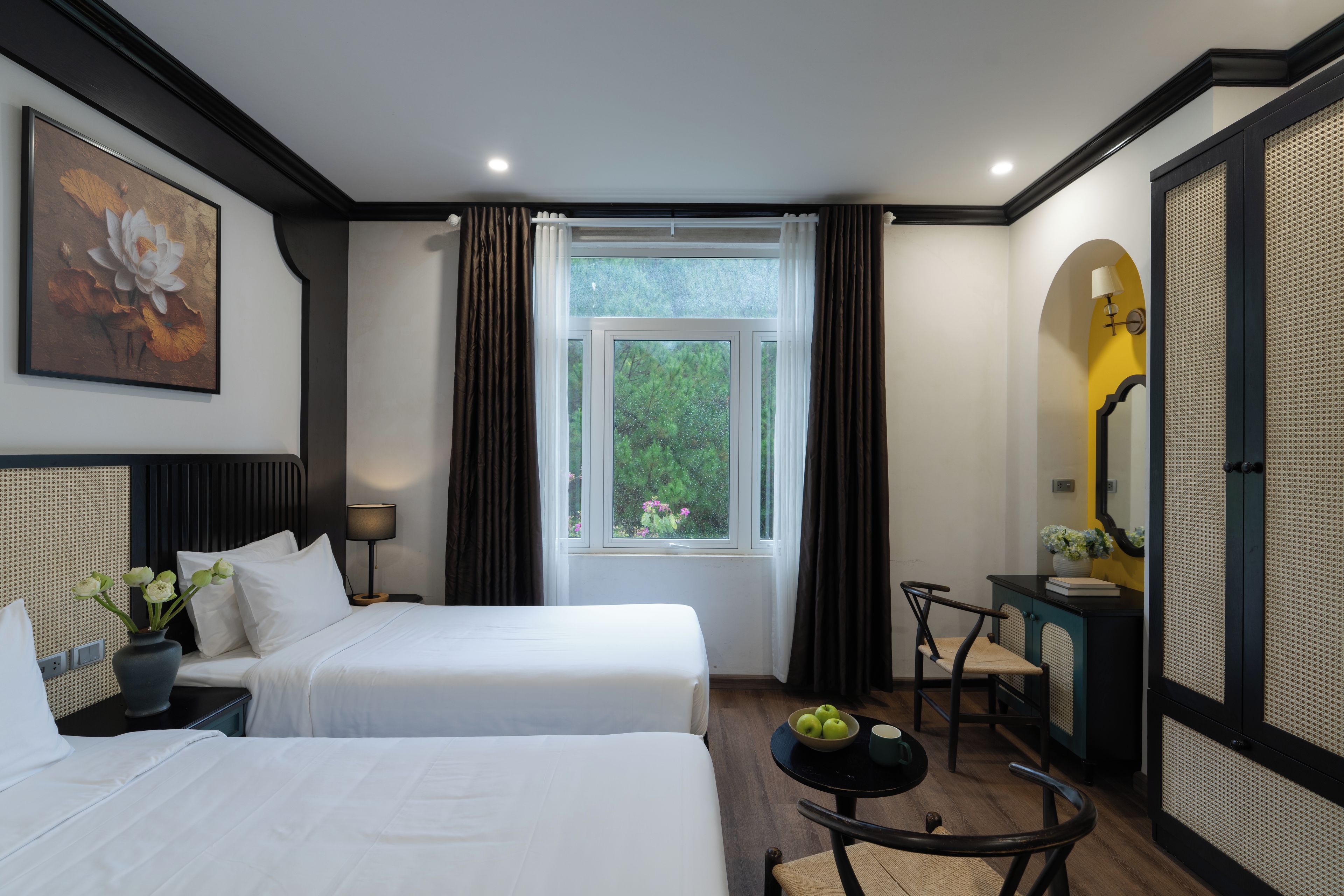 A hotel room with two beds, a window with curtains, a desk with a chair, and a painting on the wall.