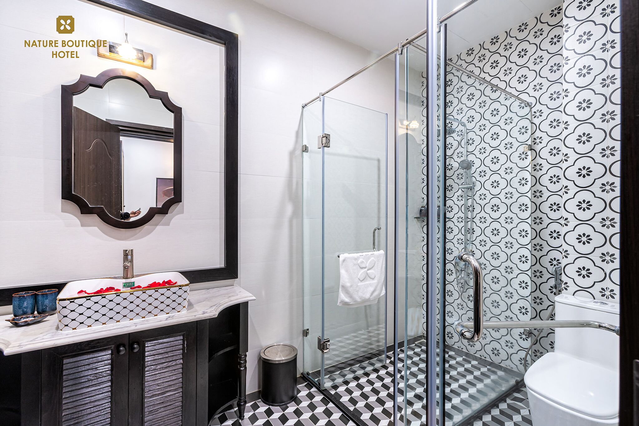 A bathroom with a glass shower enclosure, a sink with a decorative mirror, and patterned tiles.