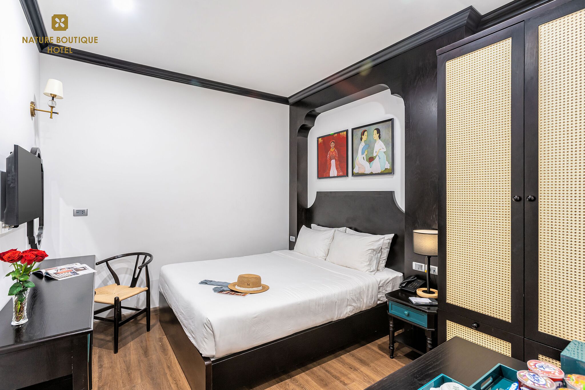 A hotel room with a bed, a desk, a chair, a TV, and artwork on the wall.