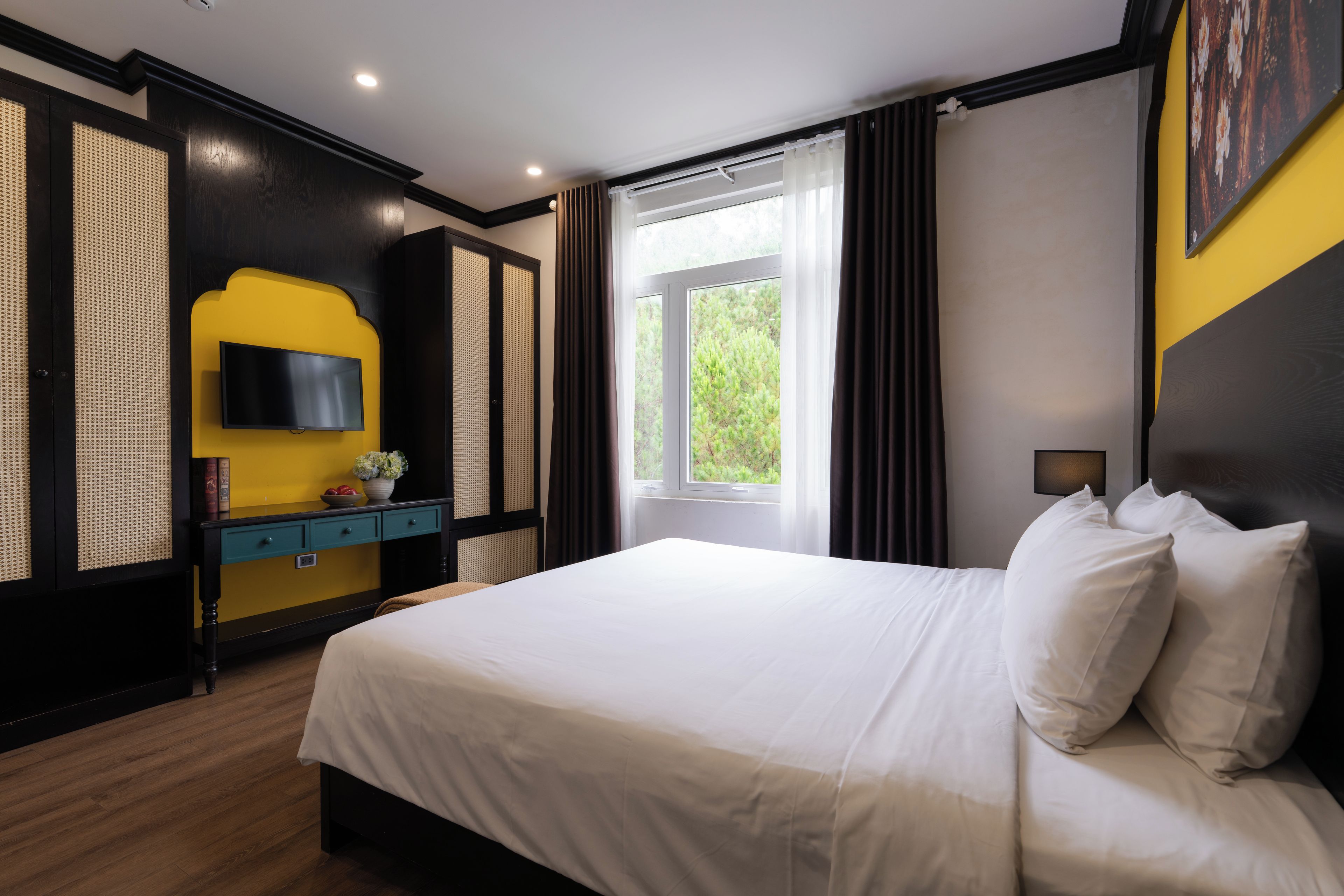 A bedroom with a bed, a TV, a window with curtains, and a view of greenery outside.