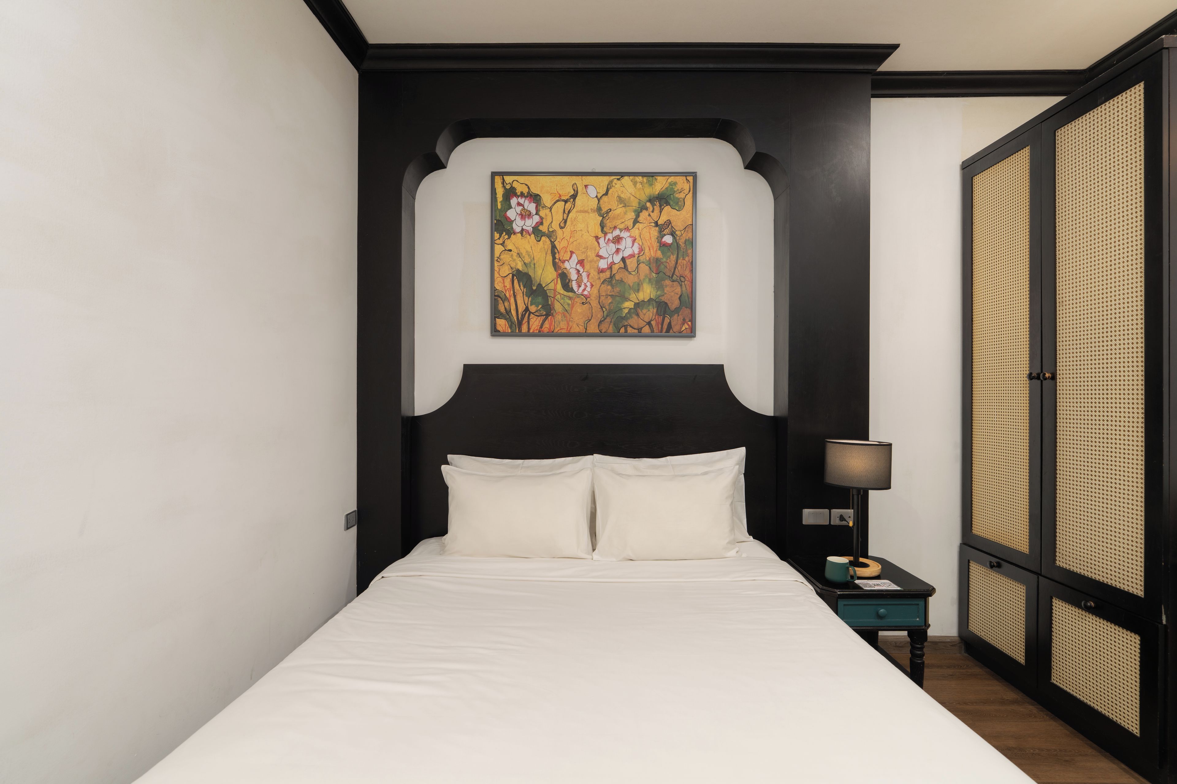 Una cama con ropa de cama blanca, un cabecero negro y un cuadro de flores colgado en la pared.