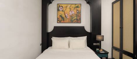 Una cama con ropa de cama blanca, un cabecero negro y un cuadro de flores colgado en la pared.