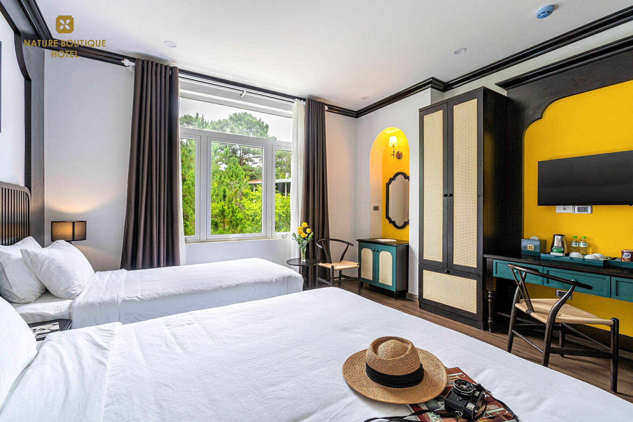 Habitación de hotel con dos camas, un escritorio, una silla, un espejo y una ventana con vistas a zonas verdes.