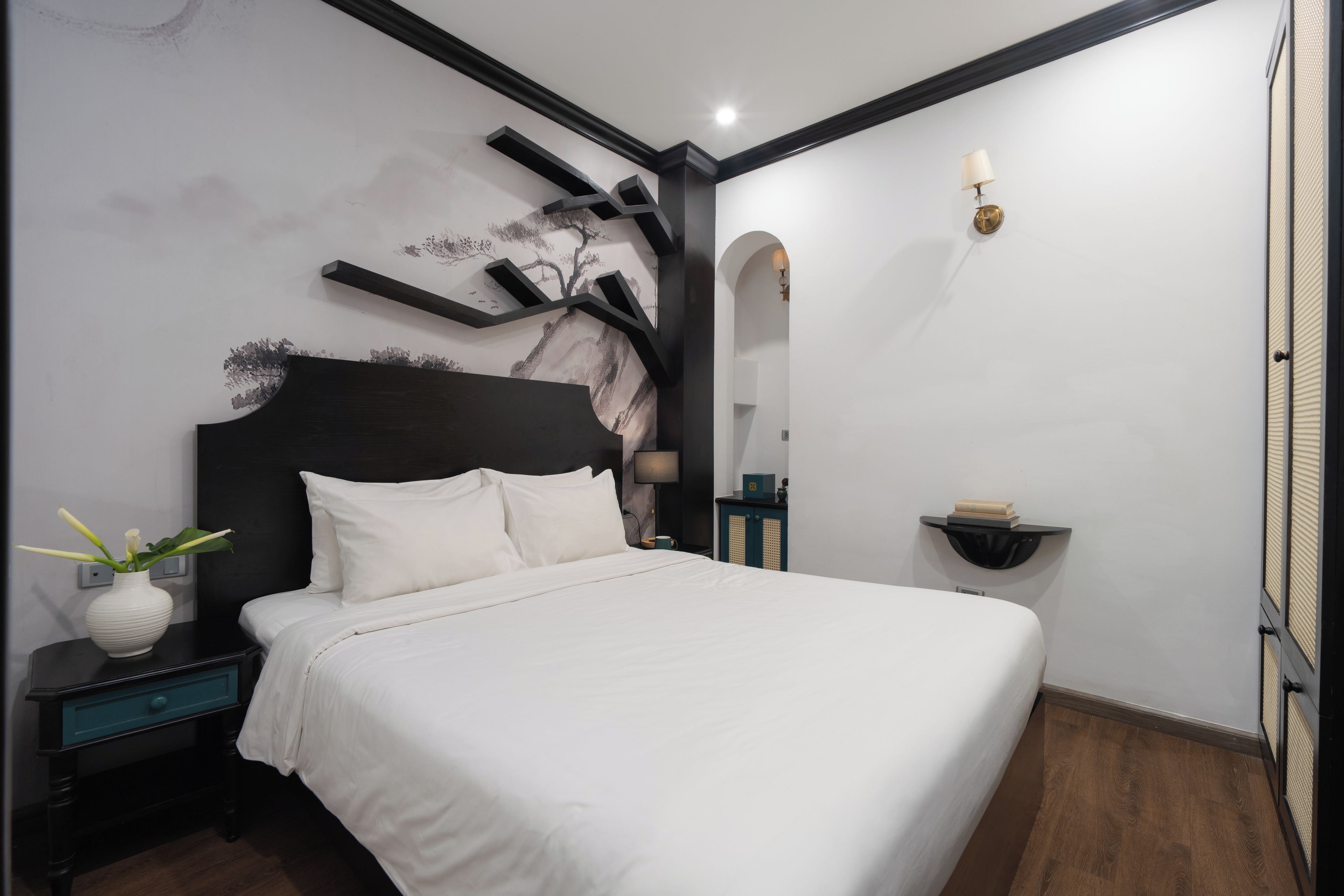A modern bedroom with a large bed, a nightstand, a wall-mounted shelf, and a decorative wall piece.