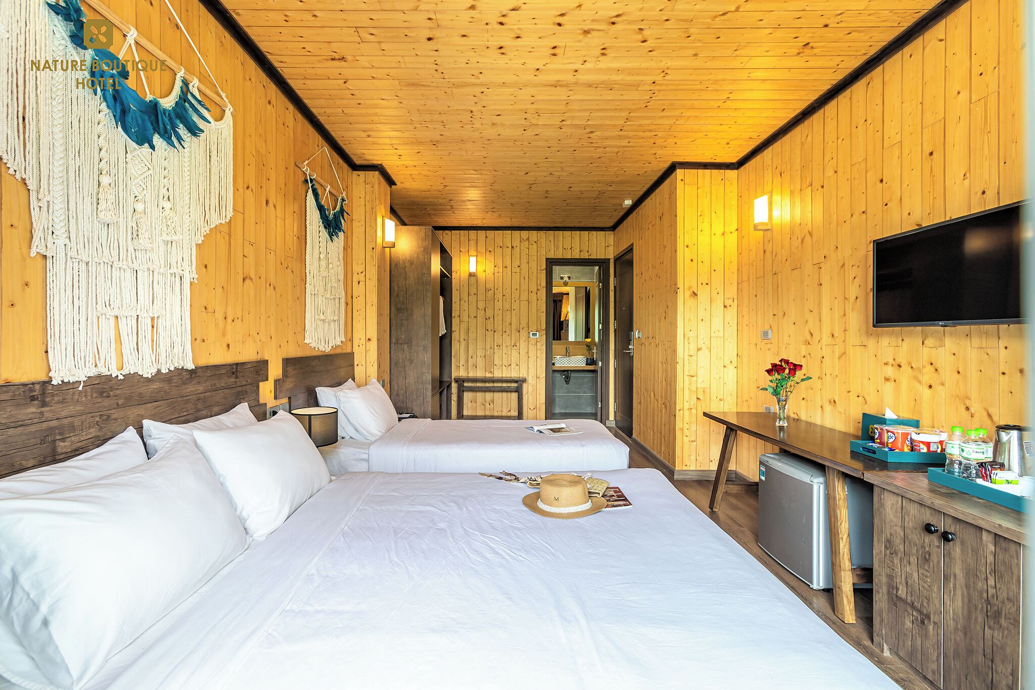 Habitación de hotel con paneles de madera, dos camas, televisor y una pequeña kitchenette.