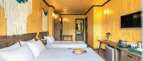 Habitación de hotel con paneles de madera, dos camas, televisor y una pequeña kitchenette.