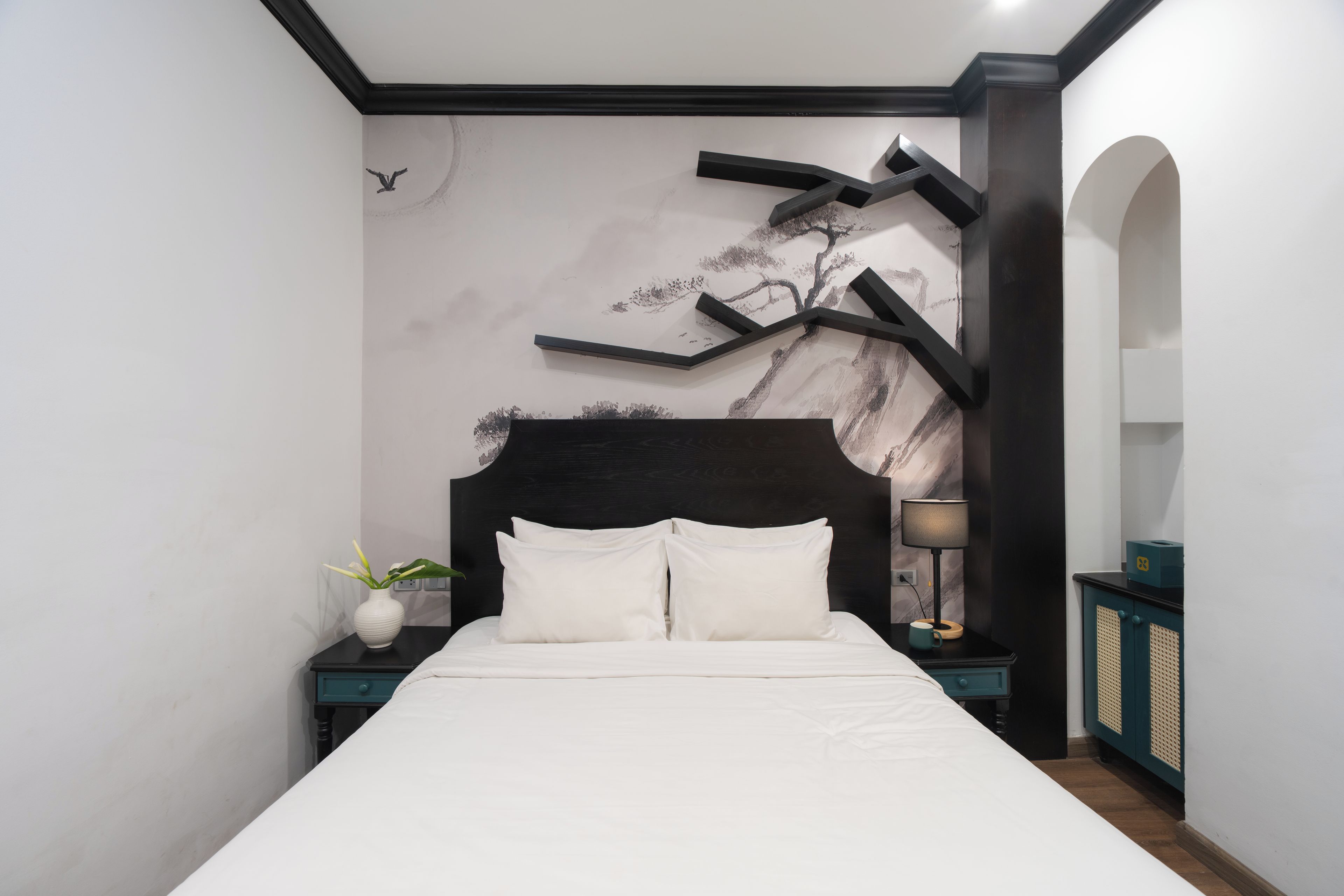 A modern bedroom with a large bed, a nightstand, a lamp, and a wall art piece.
