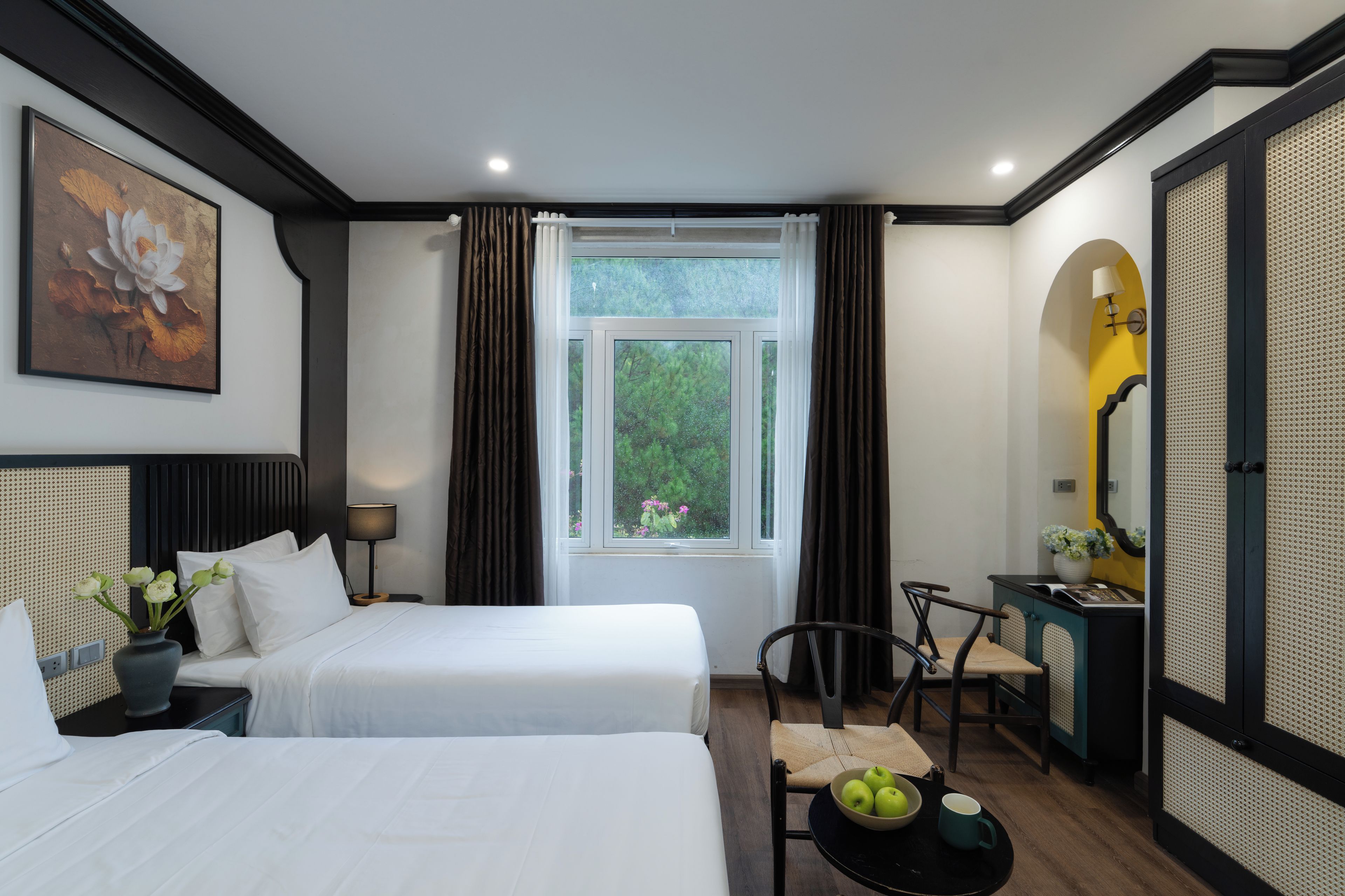 A hotel room with two beds, a desk, a chair, a window with curtains, a painting, and a lamp.