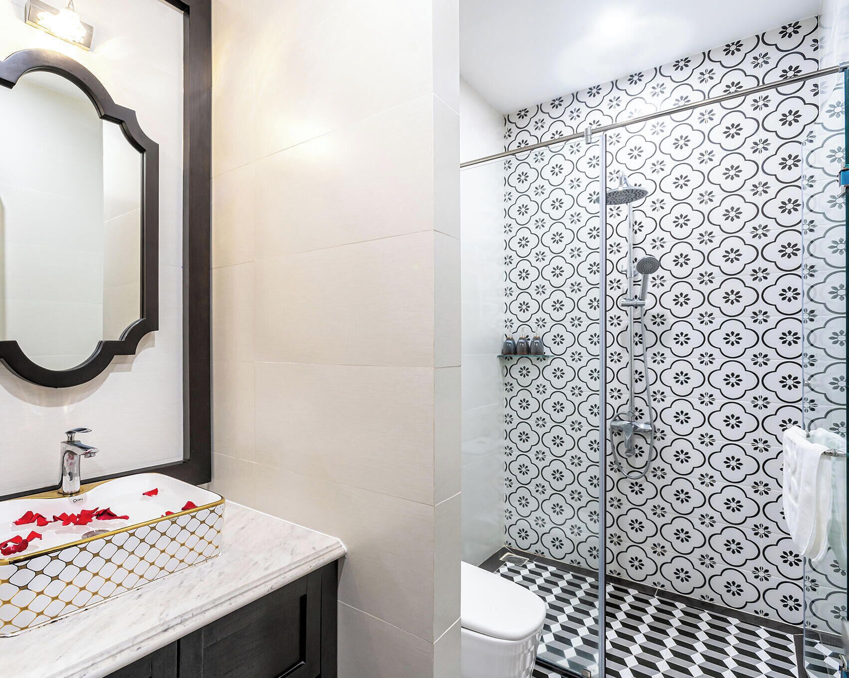 A bathroom with a white sink, mirror, and shower with black and white patterned tiles.
