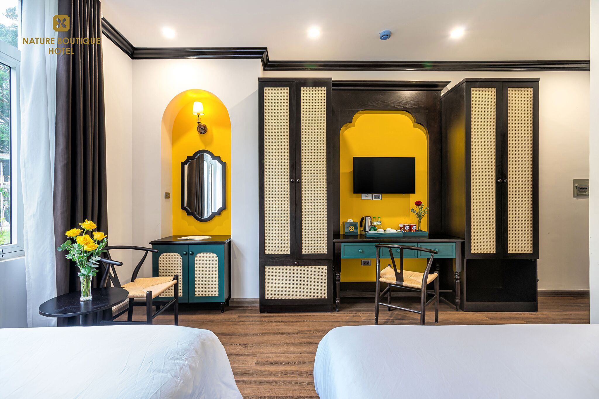 Habitación de hotel con dos camas, un escritorio con televisor, un espejo y una ventana con cortinas.